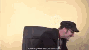 a man wearing a hat and glasses sitting in a chair