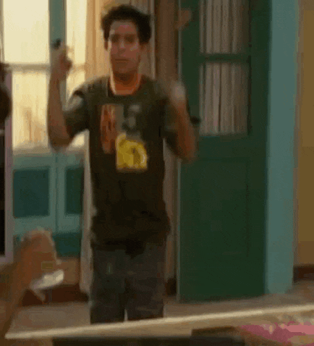a man in a black t-shirt is standing in front of a green door in a room .