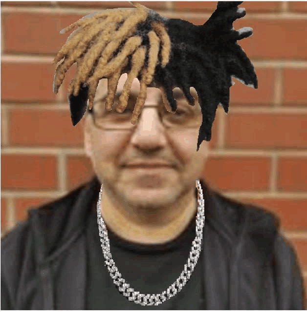 a man with dreadlocks on his head and a chain around his neck stands in front of a brick wall