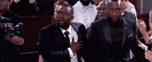 a man in a suit and tie is standing in front of a crowd of people with his hands on his chest .