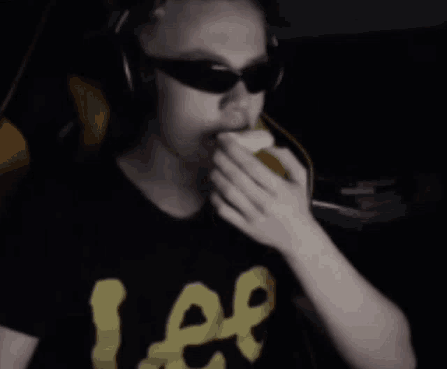 a man wearing sunglasses and a lee t-shirt eating a banana