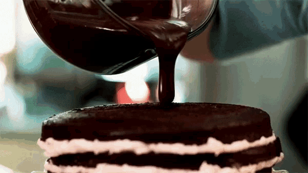 a person pouring chocolate sauce on a chocolate cake