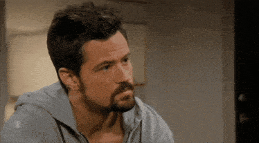 a man with a beard is wearing a grey shirt and a hoodie