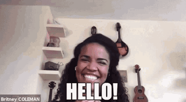 a woman is smiling and saying `` hello '' while sitting in front of a wall with guitars hanging on it .
