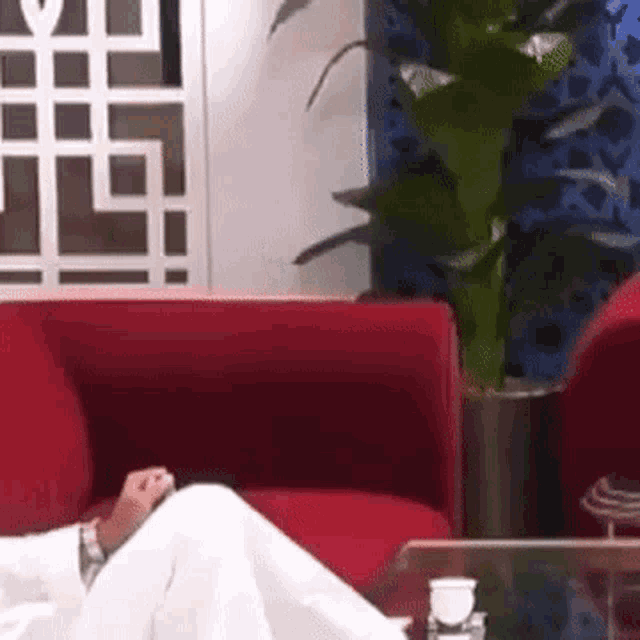 a man in a white robe is sitting on a red couch with his legs crossed .