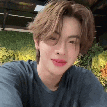 a young man wearing a blue shirt and pink lipstick is taking a picture of himself .