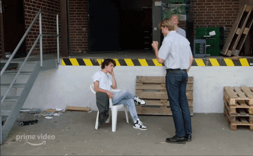 a man sits in a white chair in front of a brick building with a sign that says prime video on it