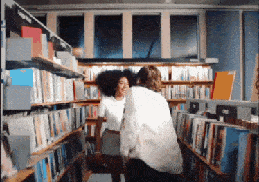 a man and a woman are standing in a library with a sign that says cine on it