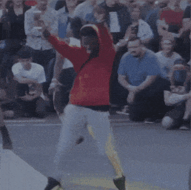 a man in a red hoodie is jumping in the air in front of a crowd of people