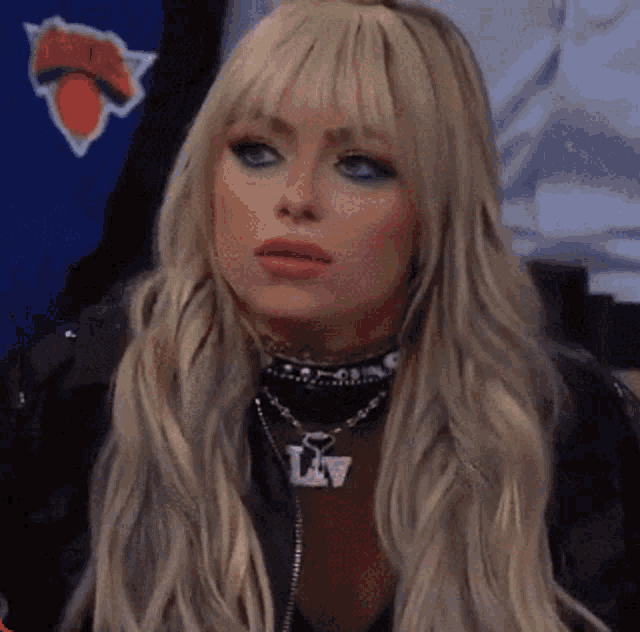 a woman wearing a necklace that says lv is sitting in front of a new york knicks logo
