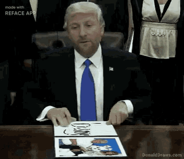 a man in a suit and tie is sitting at a table holding a book with a picture of trump on it .