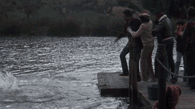 a group of people standing on a wooden dock near a body of water