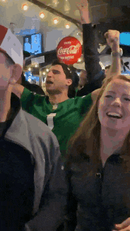 a man in a green shirt is holding a coca cola sign in his hand