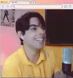 a man in a yellow shirt is smiling while sitting in front of a computer screen .