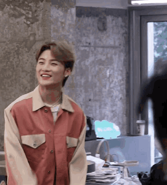 a young man wearing a pink and tan jacket is smiling in a room .