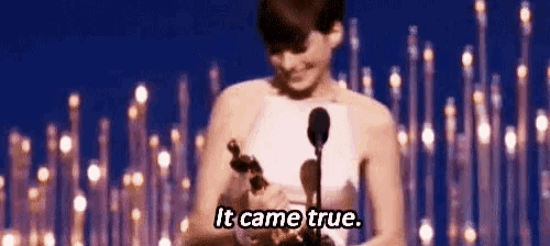 a woman is holding an oscar statue on a stage and says `` it came true '' .