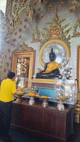 a man in a yellow shirt stands in front of a statue of buddha