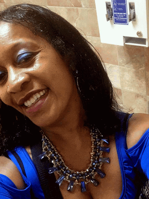 a woman wearing a blue top and a necklace smiles