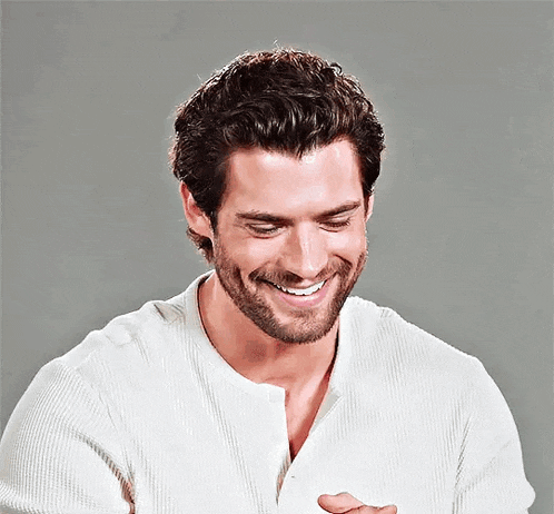 a man with a beard is smiling while wearing a white shirt .