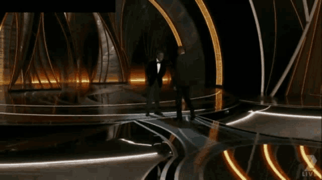 a man in a suit is walking on a stage with the words live on the bottom right