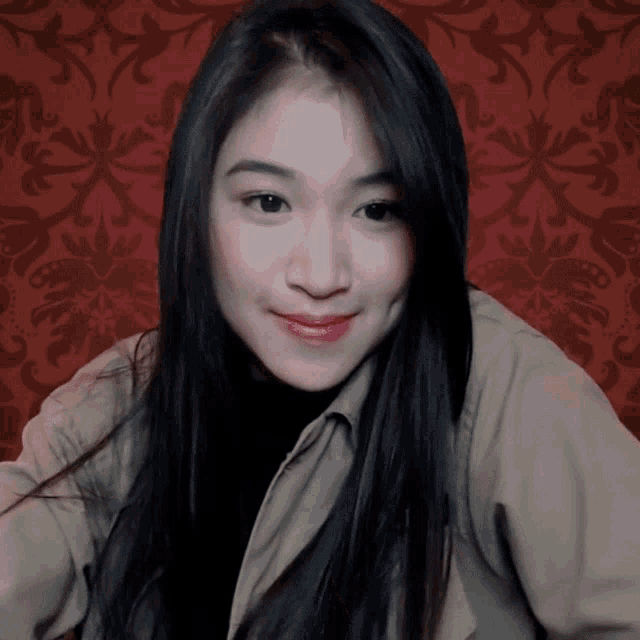 a woman with long dark hair is smiling in front of a red wall