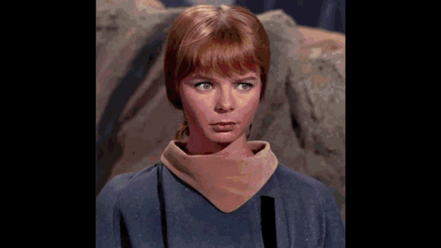 a woman with red hair is wearing a blue shirt and a brown turtleneck .