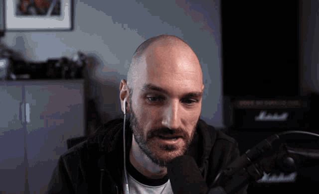 a bald man with a beard is wearing ear buds in front of a marshall amplifier