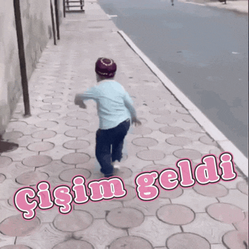 a little boy is running down a sidewalk with the words gisim geldi written on the sidewalk