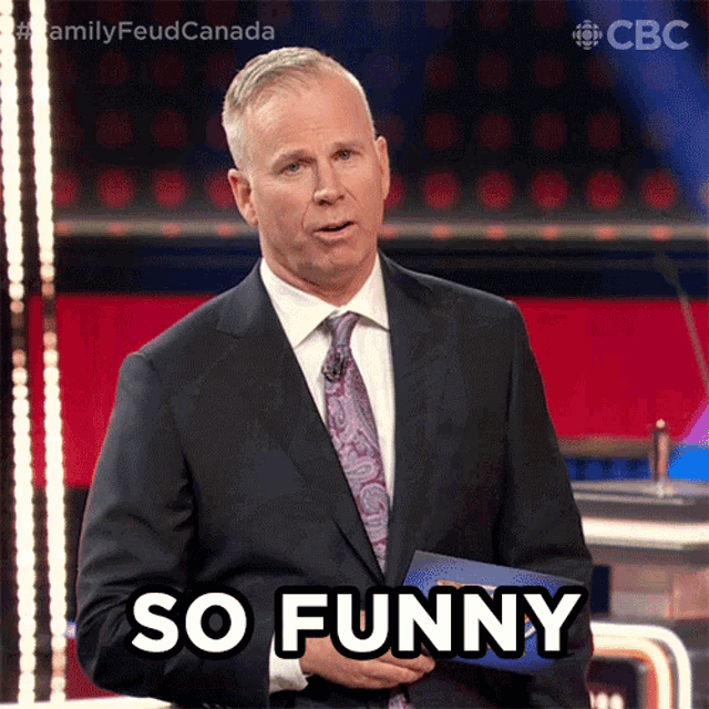 a man in a suit and tie says so funny in front of a microphone
