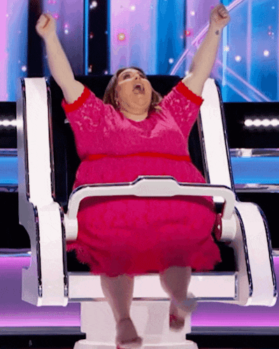 a woman in a pink dress is sitting in a chair with her arms up