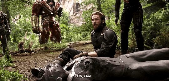 captain america sits on the ground next to a fallen iron man