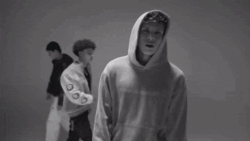 a black and white photo of a man in a hoodie standing in front of a wall .