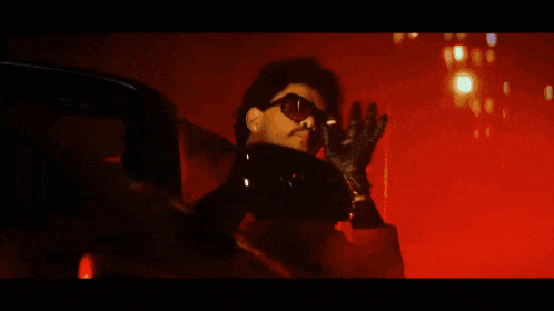 a man wearing sunglasses is smoking a cigarette in a dark room