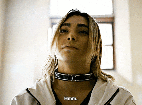 a woman wearing a choker and a white jacket says " hmm "