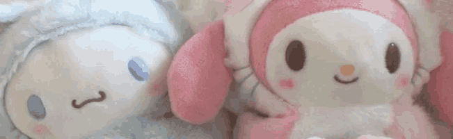 a close up of two stuffed animals , one blue and one pink , sitting next to each other on a bed .