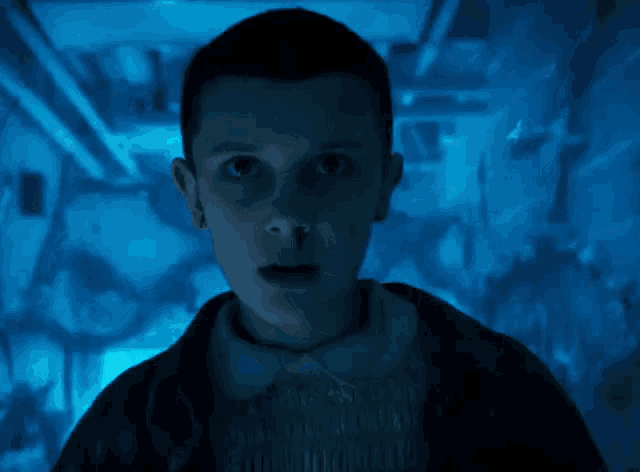 a close up of a person 's face in a dark room with a blue light behind them