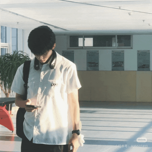 a man in a white shirt is looking at his phone in a room
