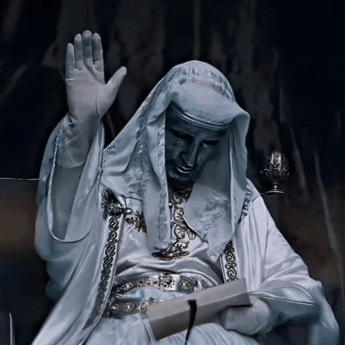 a statue of a man in a white robe is reading a book and waving his hand