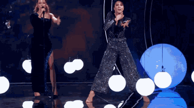 a woman singing into a microphone next to another woman dancing