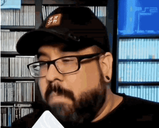a man with a beard and glasses is wearing a hat and holding a microphone .