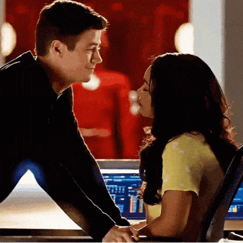 a man and a woman are looking at each other and kissing in front of a computer screen .