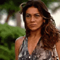 a woman in a floral dress is standing in front of a bush .