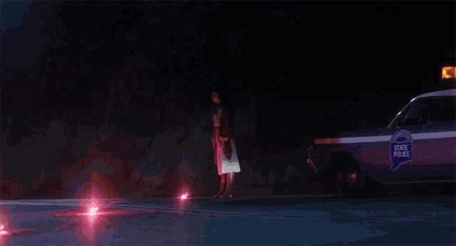 a woman stands next to a state police car