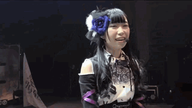 a girl with a flower in her hair is wearing a microphone and smiling on a stage .