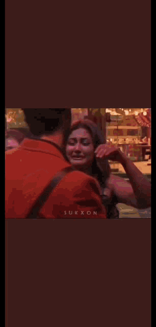 a man in a red shirt is hugging a woman in a white tank top