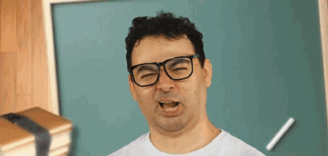 a man wearing glasses is making a funny face in front of a chalkboard