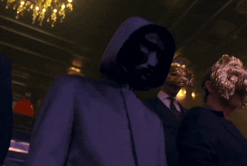 a man in a hooded jacket stands in a dark room with other people