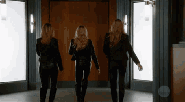 three women are walking down a hallway with abc written on the wall behind them