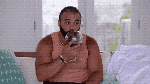 a man is sitting on a couch drinking from a glass .