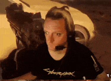 a man wearing headphones and a cyberpunk t-shirt is sitting in front of a car .